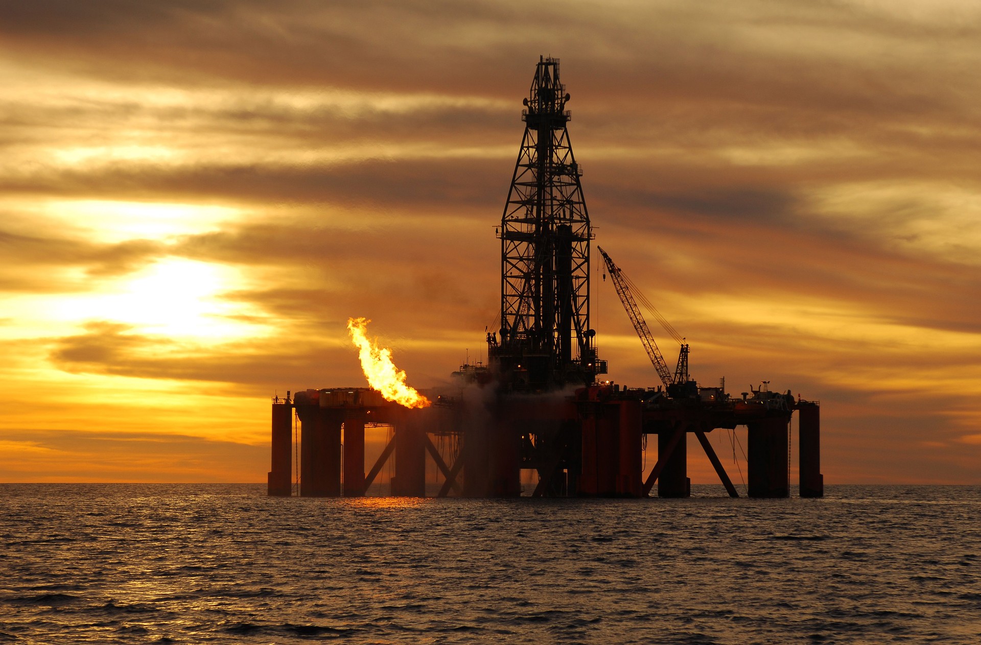 Silhouette of ocean oil rig at sunset.